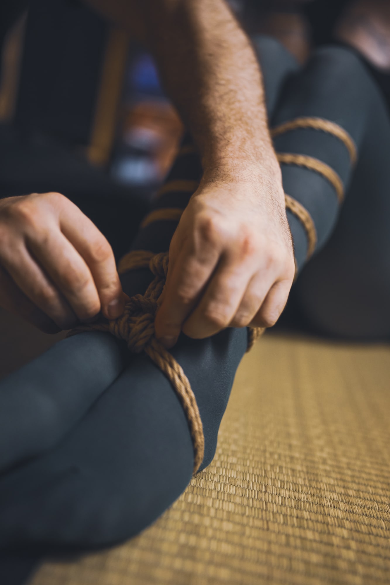 Detail rukou lektora při vázání uzlu na nohou během praxe na tatami.